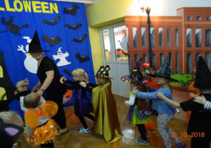 Na tle dekoracji halloweenowej dzieci tańczą z nauczycielką po kole.